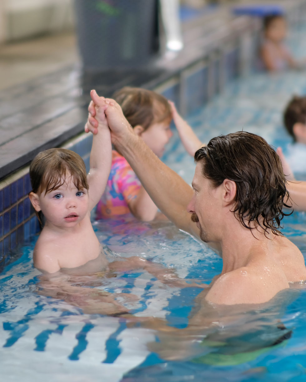 Father supporting his son during Dippas baby swimming lesson at Superfish Swim Schools indoor heated pool